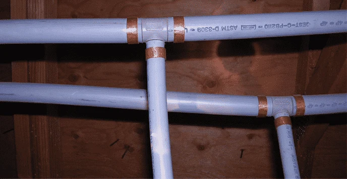Grey polybutylene water pipes under a floor, joined with grey plastic fittings and copper crimp rings, with PB2110 printed on the pipe